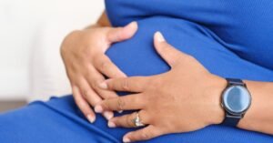 Mulher grávida sentada com as duas mãos apoiadas sobre a barriga