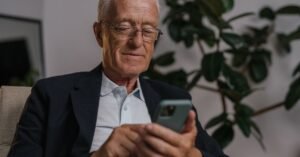 Homem idoso de óculos usa o celular sentado em uma poltrona