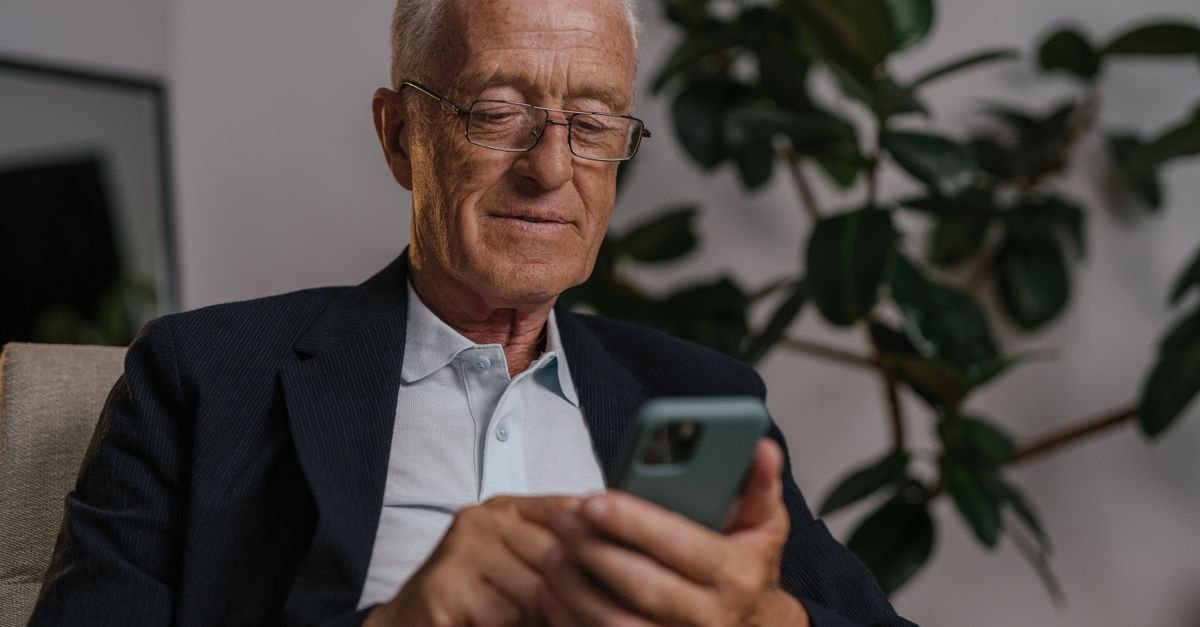 Homem idoso de óculos usa o celular sentado em uma poltrona