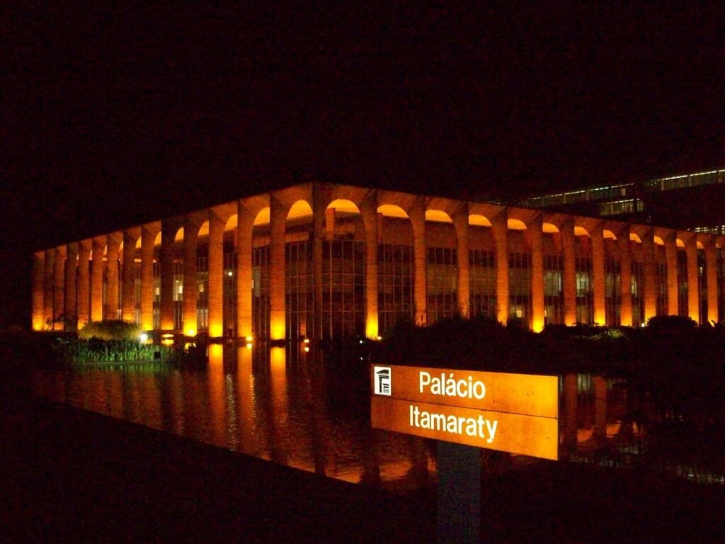Fachada iluminada do Palácio Itamaraty à noite com placa de identificação