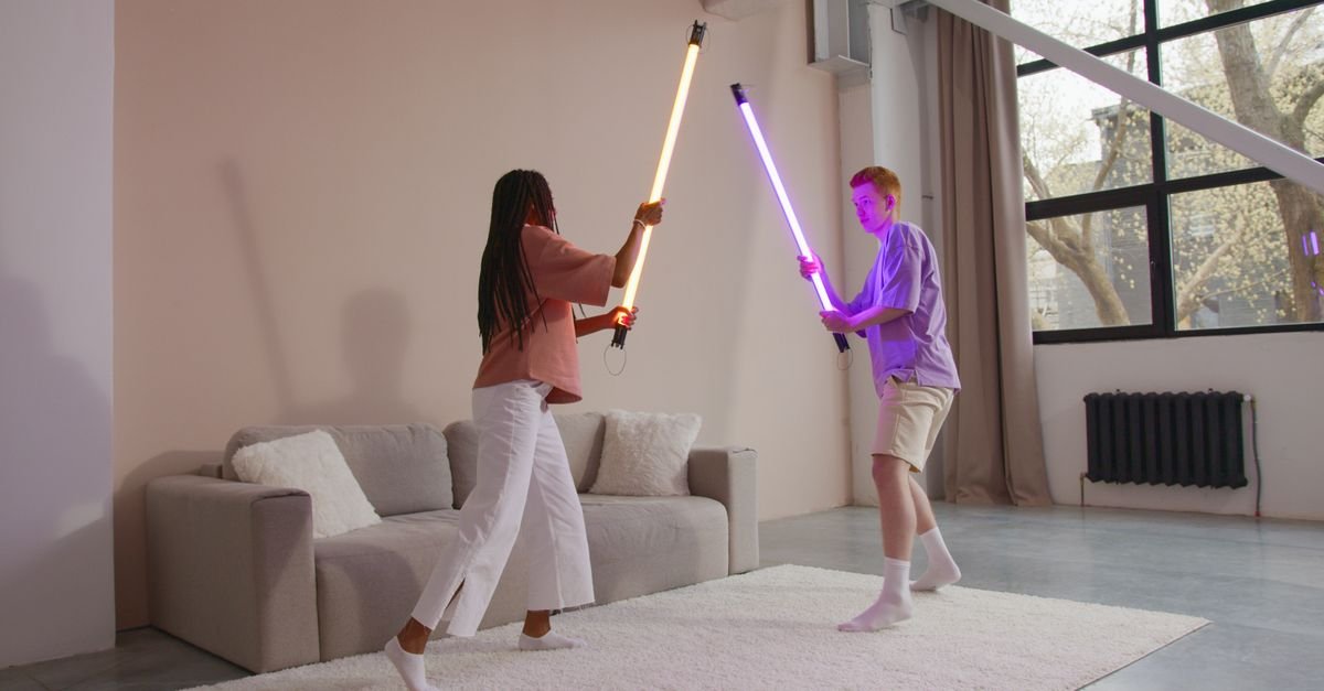 Duas pessoas empunham sabres de luz de LED, um laranja e um roxo, em uma sala