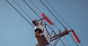 Eletricista com capacete amarelo trabalha em cesto aéreo sobre rede de distribuição de energia