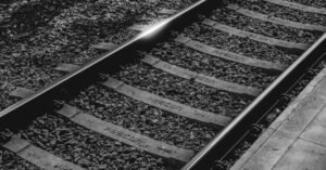 Trilhos ferroviários com dormentes de concreto e lastro de brita em imagem preto e branco