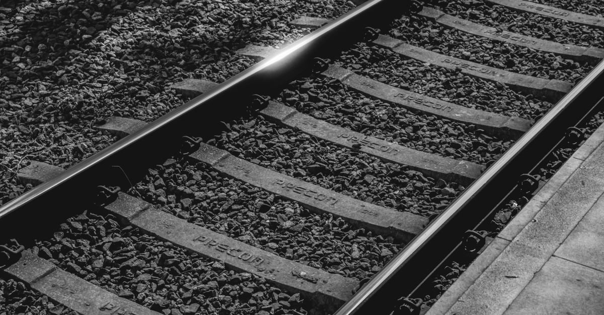 Trilhos ferroviários com dormentes de concreto e lastro de brita em imagem preto e branco