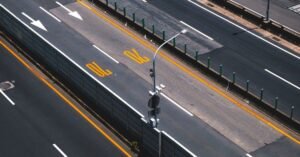 Vista aérea de pista de rodovia com faixas amarelas e brancas, setas de sinalização e poste de iluminação