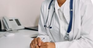 Profissional de jaleco branco com estetoscópio ao pescoço sentado à mesa de consultório