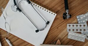 Estetoscópio sobre caderno, ao lado de óculos e cartelas de comprimidos