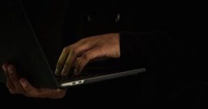 Mãos digitam em notebook em ambiente escuro, sem rosto visível