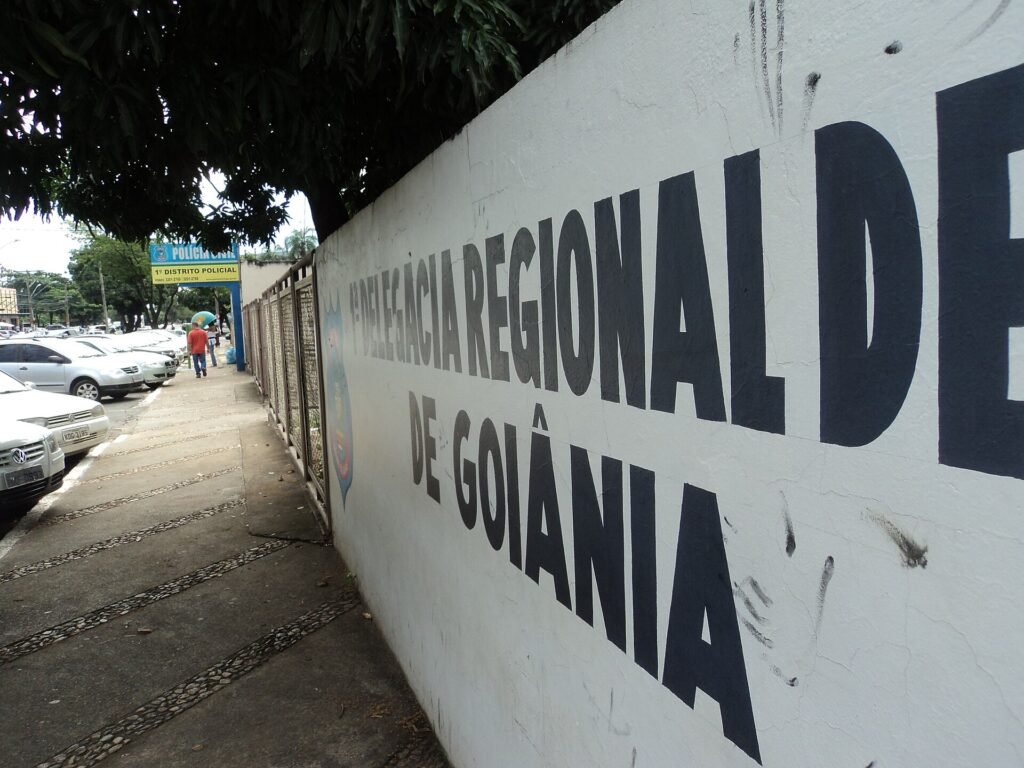 Fachada de delegacia da Polícia Civil de Goiás, com muro branco e letreiro em letras pretas