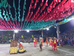 Casal de dançarinos de quadrilha junina em arena decorada com bandeirinhas coloridas