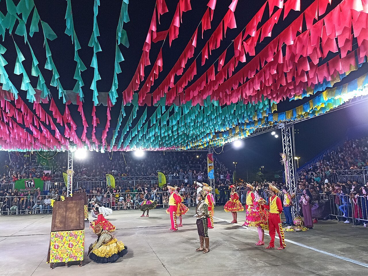 Casal de dançarinos de quadrilha junina em arena decorada com bandeirinhas coloridas