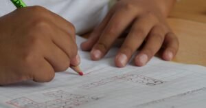 Mãos de criança escrevendo com lápis em caderno quadriculado
