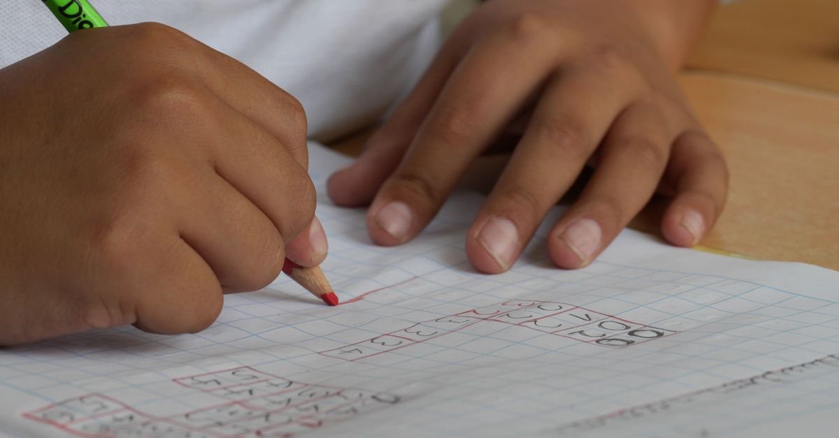 Mãos de criança escrevendo com lápis em caderno quadriculado