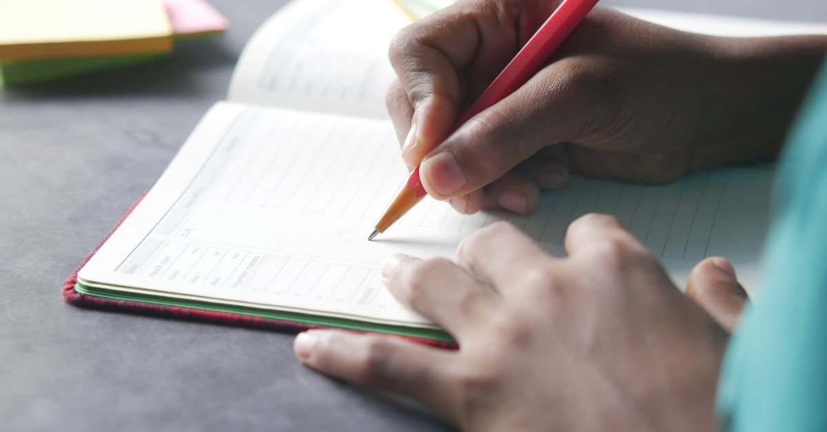 Mão de pessoa escrevendo com caneta em um caderno sobre a mesa