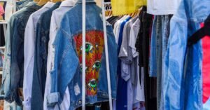 Jaquetas jeans e camisetas penduradas em araras de um bazar de roupas