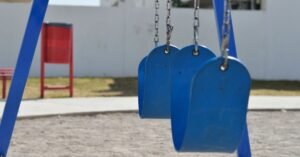 Balanços azuis vazios em parquinho com piso de areia