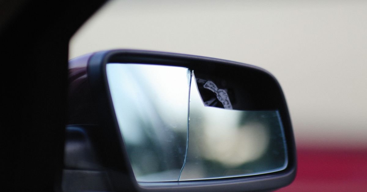 Retrovisor lateral de carro com o espelho quebrado e trincado em primeiro plano