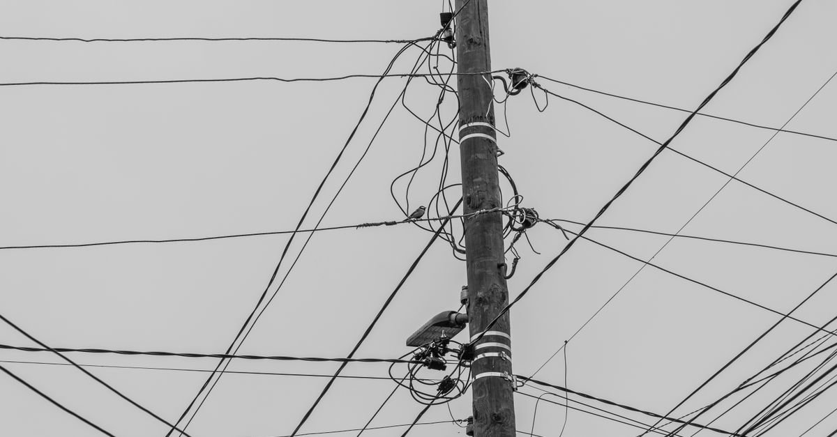 Poste de madeira com emaranhado de fios elétricos contra o céu cinza