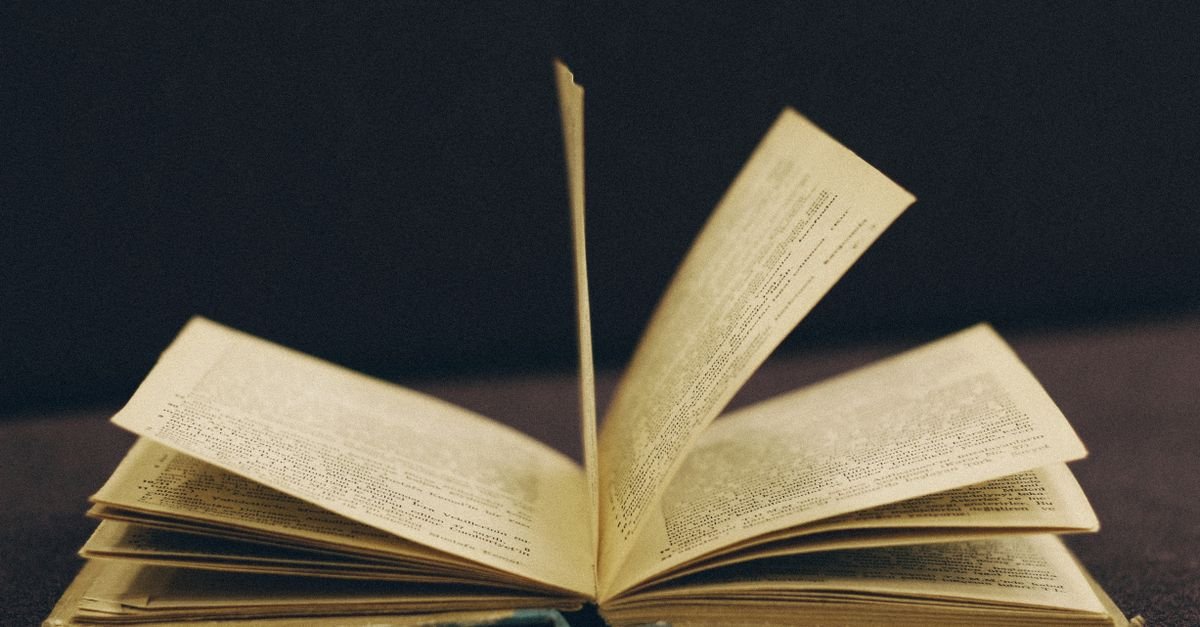 Livro antigo aberto com as páginas em meio a um movimento de virada