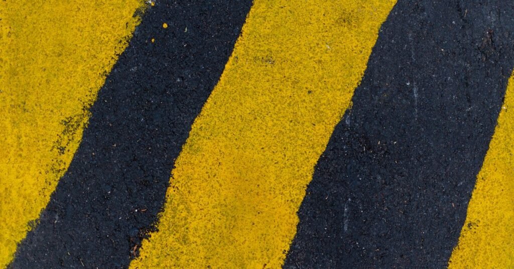 Faixas amarelas de sinalização pintadas sobre o asfalto, vistas de cima em enquadramento fechado