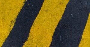 Faixas amarelas de sinalização pintadas sobre o asfalto, vistas de cima em enquadramento fechado