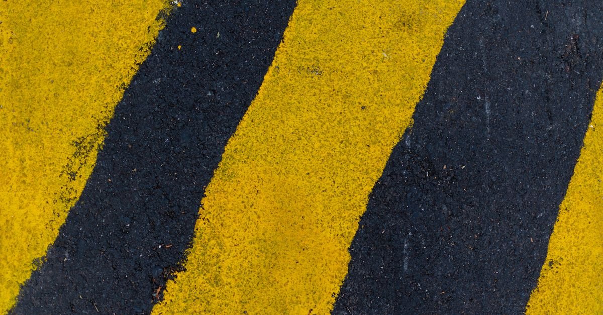 Faixas amarelas de sinalização pintadas sobre o asfalto, vistas de cima em enquadramento fechado