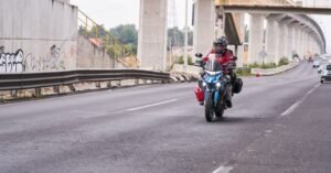 Motociclista com capacete trafega em via urbana sob viaduto de concreto, com guard-rail na lateral da pista