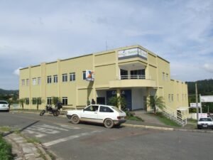 Fachada de agência da Caixa Econômica Federal com carro e moto estacionados em frente