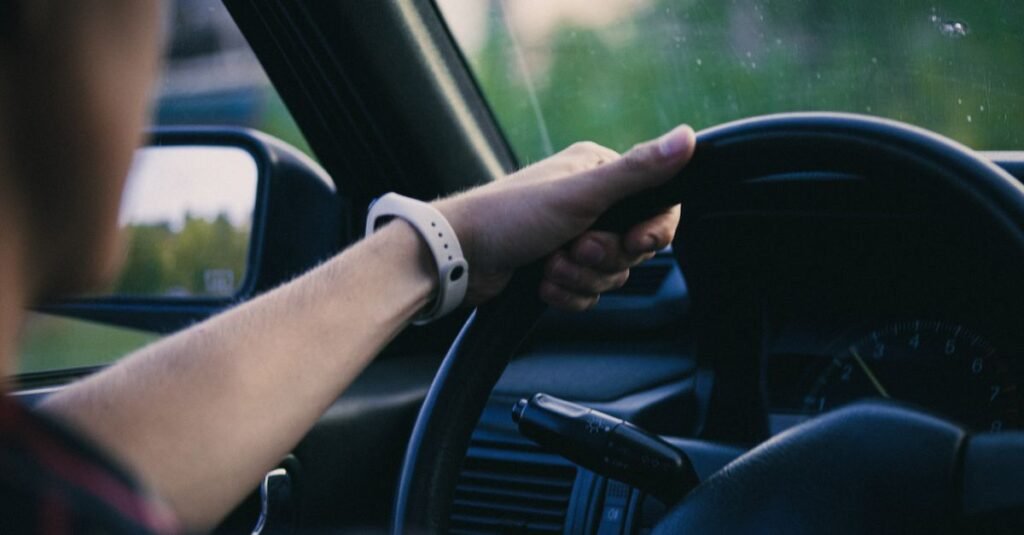 Mão de motorista apoiada no volante durante a condução, com o painel do carro ao fundo