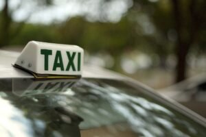 Luminoso de táxi branco e verde no teto de um carro, com árvores desfocadas ao fundo
