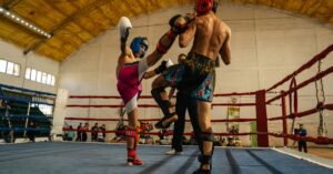 Dois lutadores de muay thai trocam golpes em um ringue durante competição em ginásio