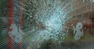 Vidro estilhaçado com trincas em formato radial ao redor do ponto de impacto