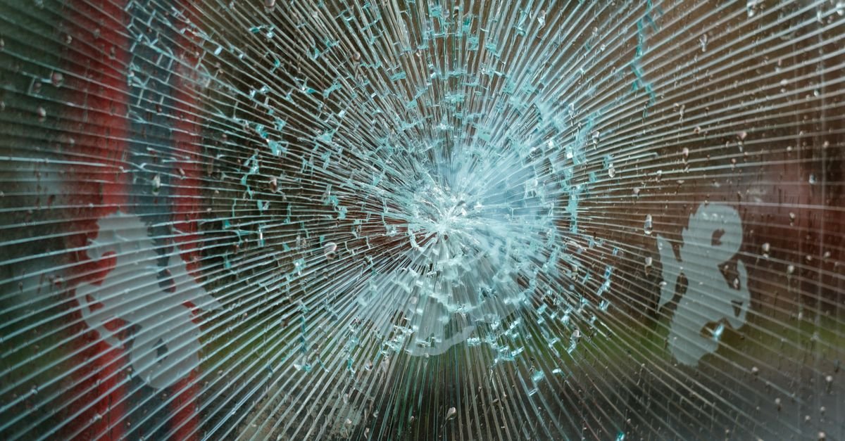 Vidro estilhaçado com trincas em formato radial ao redor do ponto de impacto
