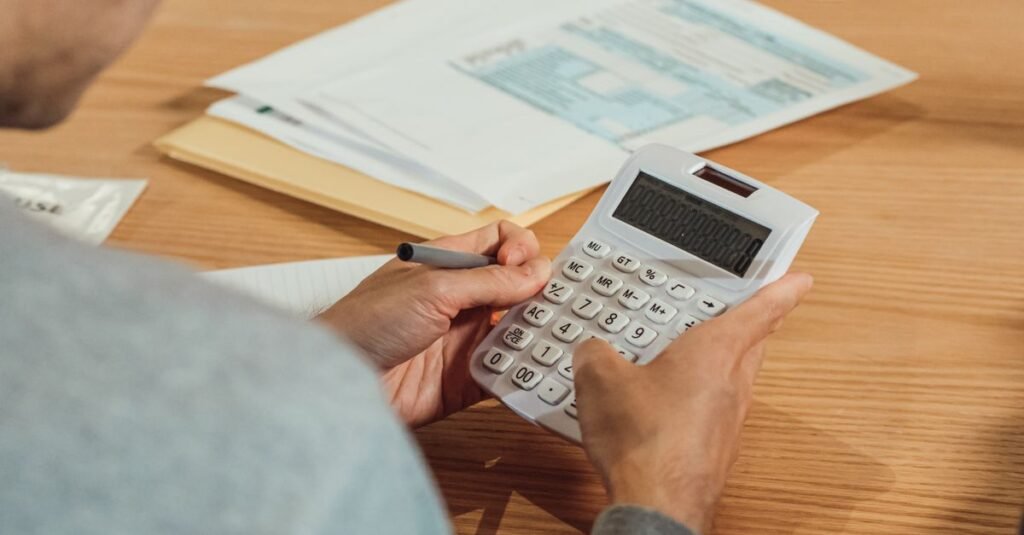 Pessoa usa calculadora sobre mesa com documentos fiscais e caneta
