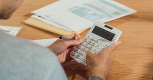 Pessoa usa calculadora sobre mesa com documentos fiscais e caneta