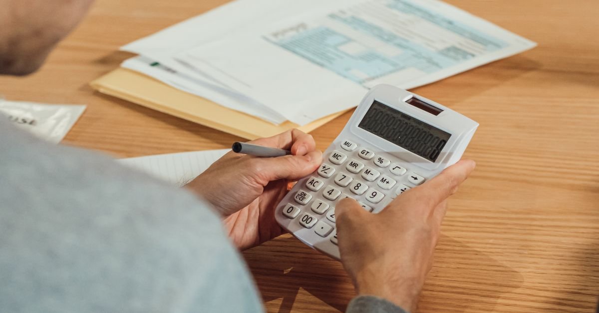 Pessoa usa calculadora sobre mesa com documentos fiscais e caneta