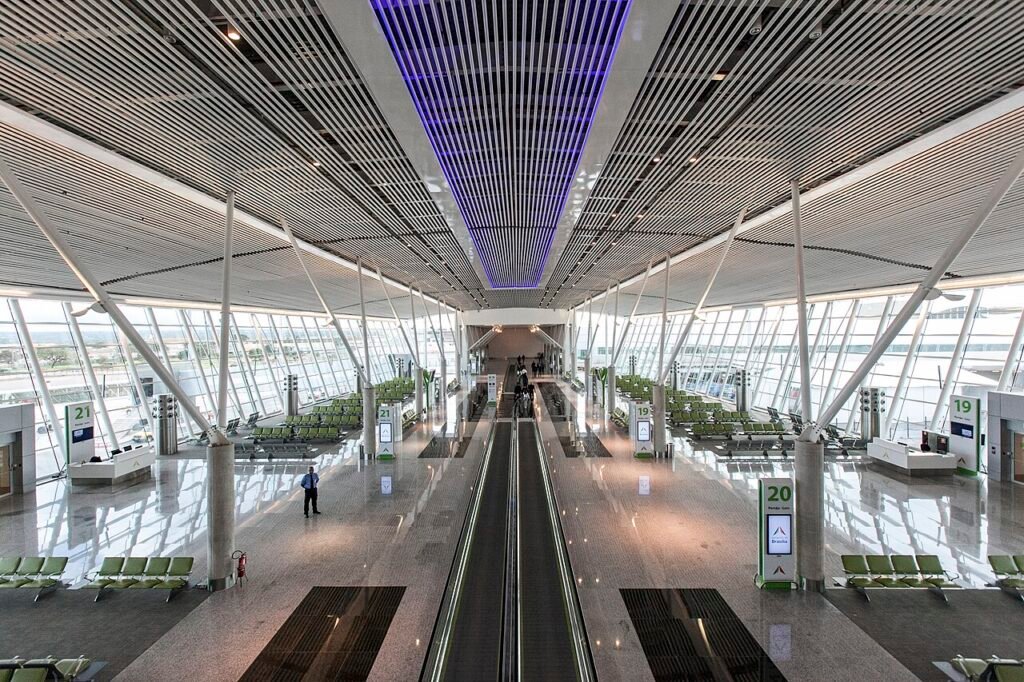 Saguão do Aeroporto de Brasília com esteira rolante central, poltronas e placas dos portões 19, 20 e 21
