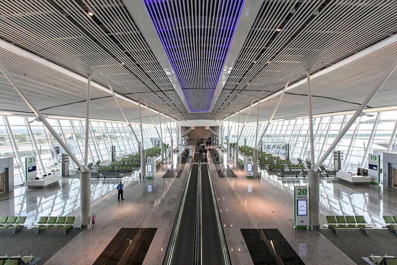 Saguão do Aeroporto de Brasília com esteira rolante central, poltronas e placas dos portões 19, 20 e 21