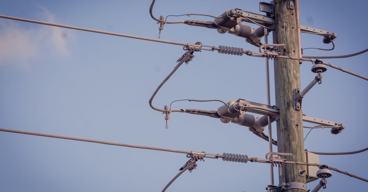 Poste de energia elétrica com fiação e isoladores contra o céu azul