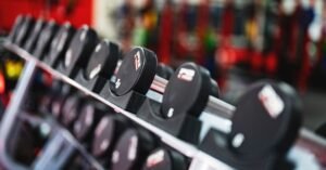 Halteres enfileirados em suporte de academia, com equipamentos desfocados ao fundo