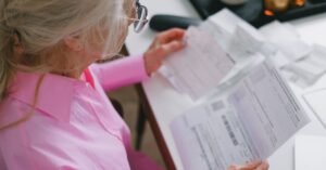 Mulher idosa de óculos lendo documentos impressos sobre uma mesa