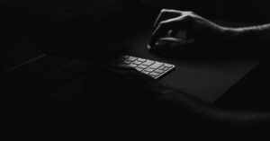 Mão sobre teclado de computador em ambiente escuro, em foto preto e branco