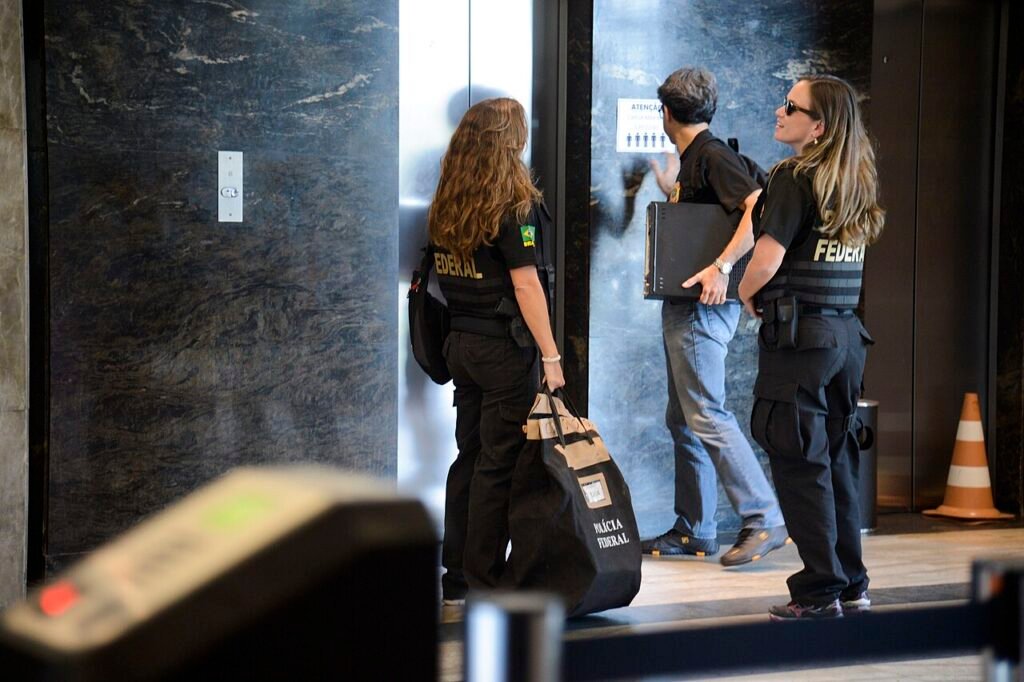 Agentes da Polícia Federal com coletes de identificação carregam material apreendido durante cumprimento de mandado