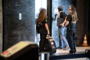 Agentes da Polícia Federal com coletes de identificação carregam material apreendido durante cumprimento de mandado