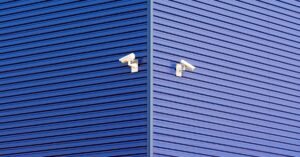 Duas câmeras de segurança instaladas na fachada azul de um prédio comercial