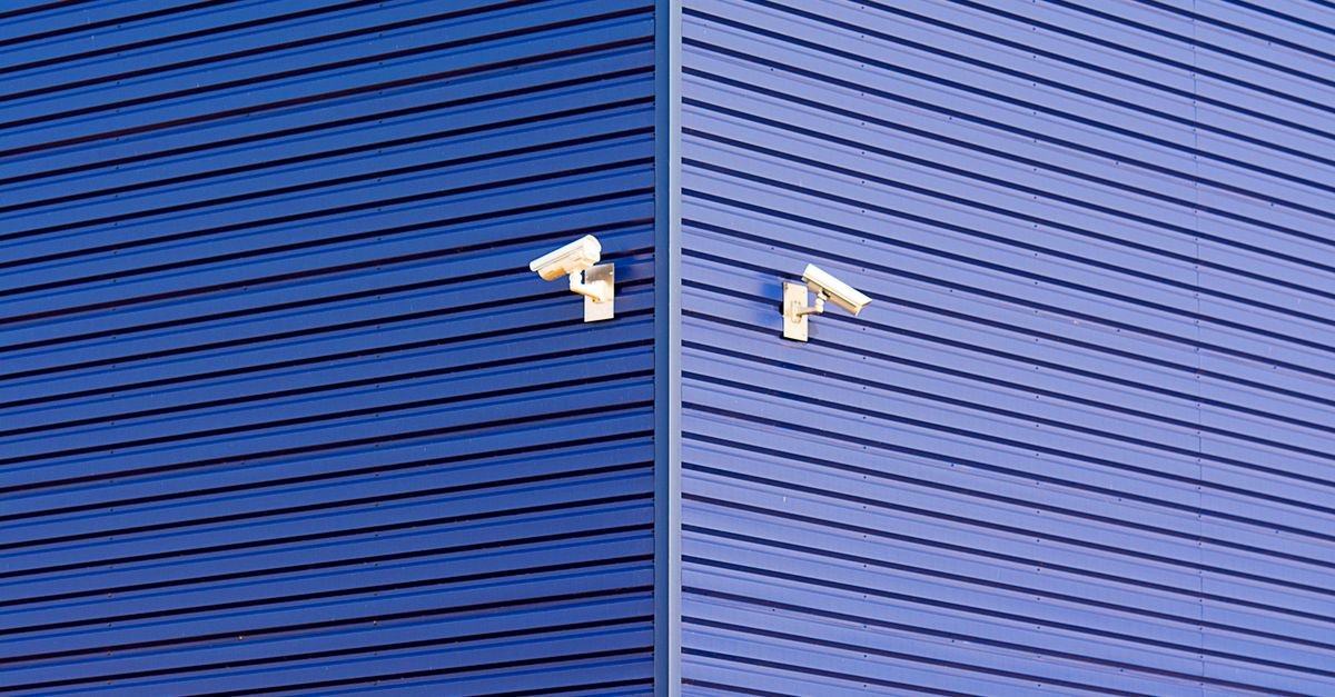 Duas câmeras de segurança instaladas na fachada azul de um prédio comercial