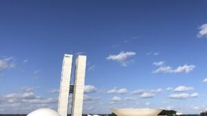 Torres do Congresso Nacional e a cúpula do plenário do Senado vistas de baixo, sob céu azul com nuvens