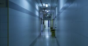 Corredor vazio de unidade de saúde com paredes de azulejo claro e iluminação fria