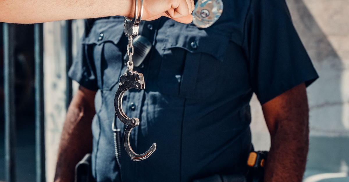 Policial uniformizado segura um par de algemas abertas em primeiro plano
