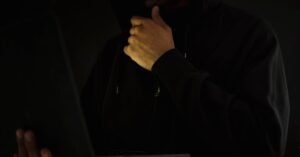 Homem de capuz usa notebook no escuro, imagem que ilustra fraude eletrônica